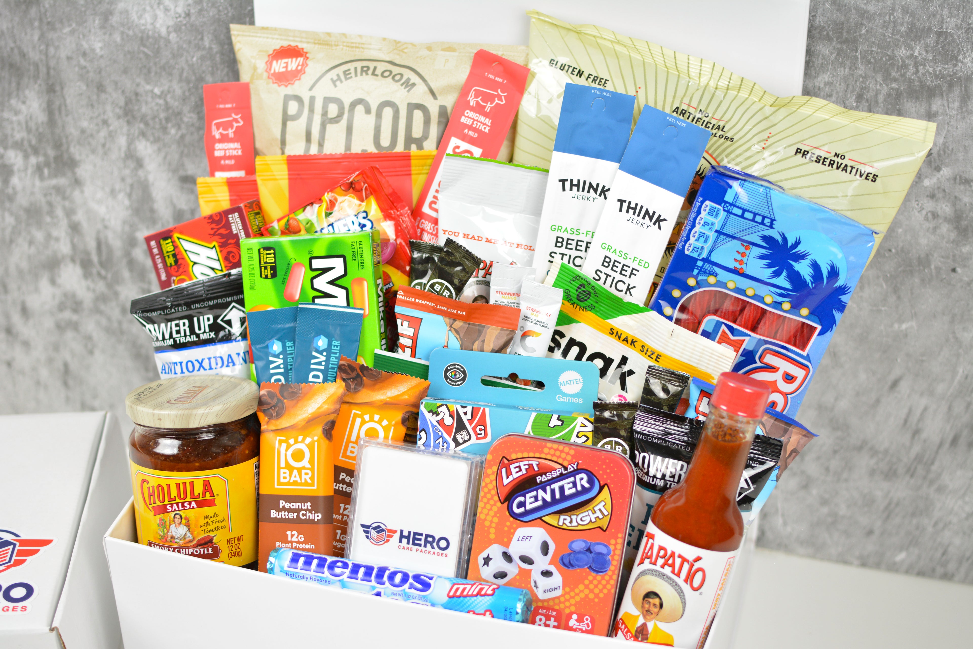 Close-up of troop-sized military care package contents, including premium snacks, UNO Team, playing cards, and Left Right Center dice game